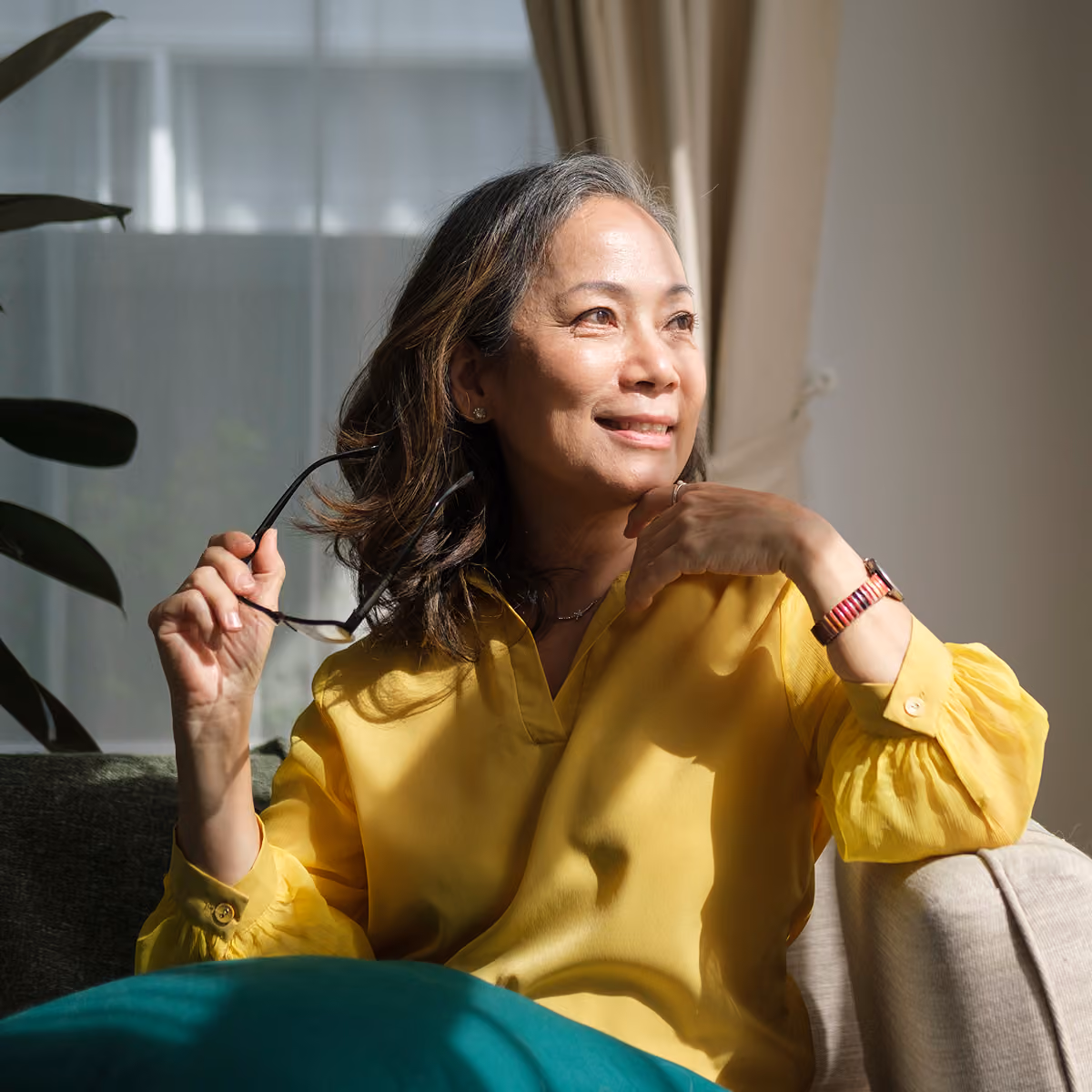 A senior woman stares out in the window looking optimistic.