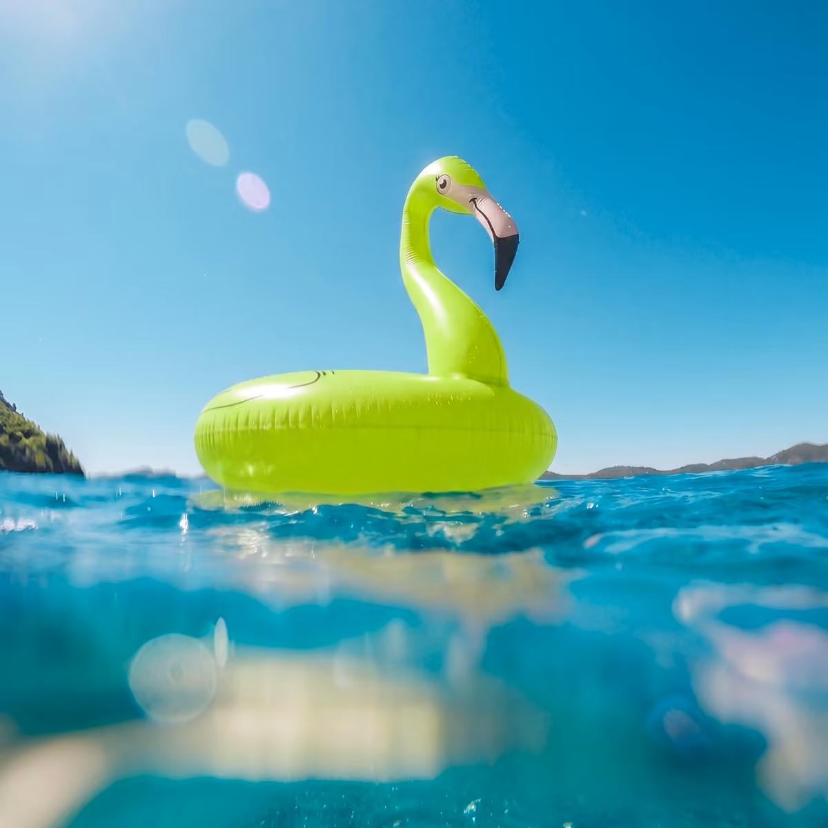 A neon green green flamingo floatie on top of crystal clear water.