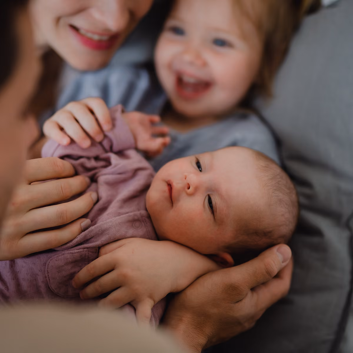 Family holds their newborn baby while resting on their bed.