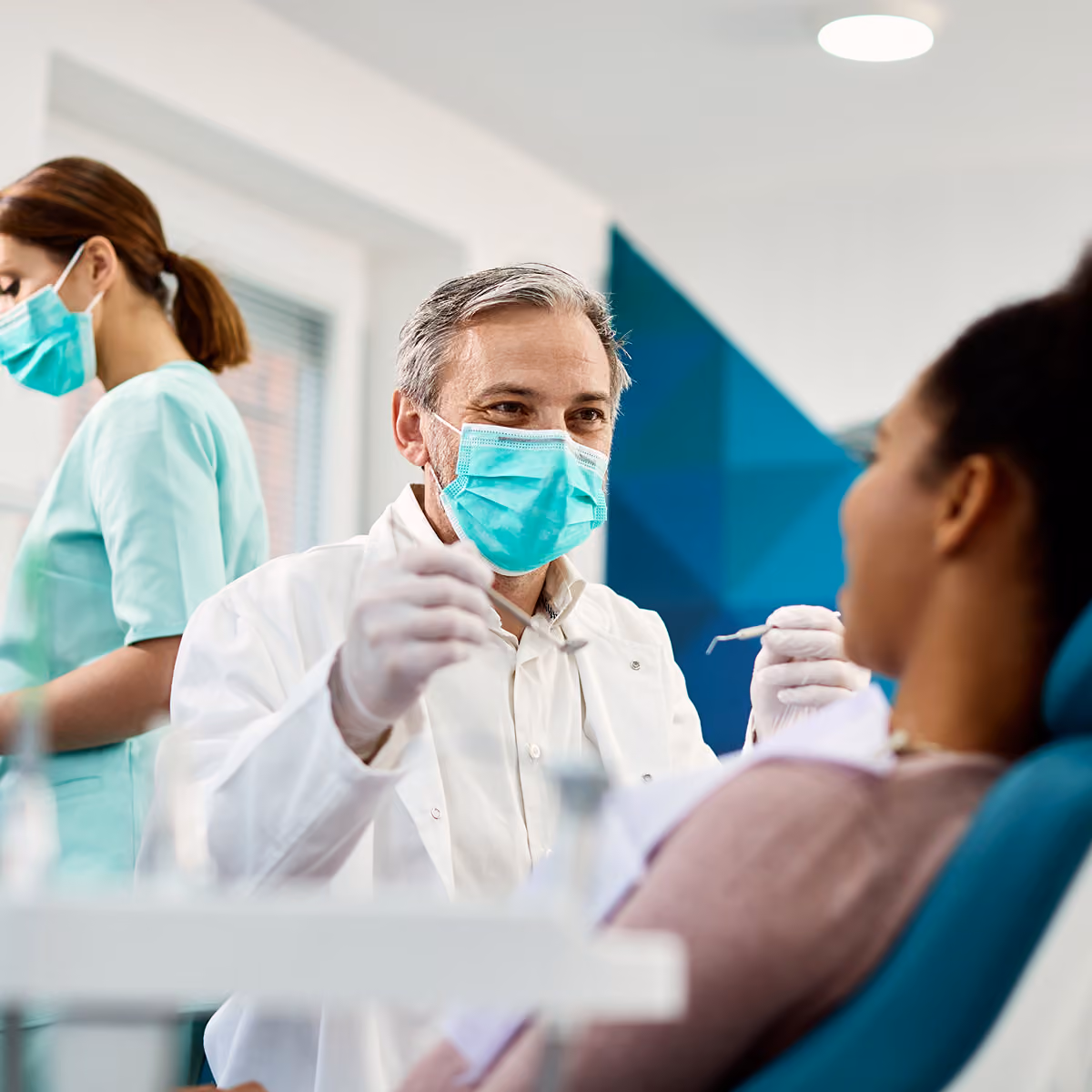 A dentist performing a cleaning on a woman sitting in a dentist chair.
